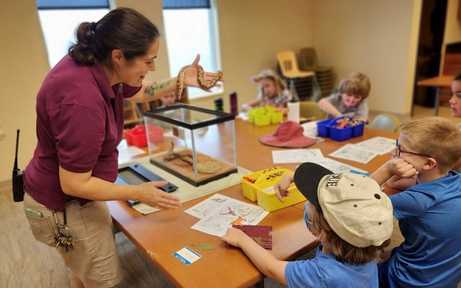 Educator holds small snake in front of classroom of children